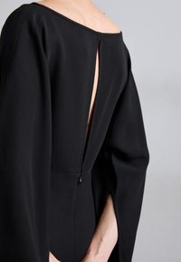 Black dress featuring a wide off-the-shoulder neckline, a deep back opening, and flared sleeves with a subtle slit. Smooth fabric texture.