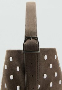 Sac en suède marron avec une finition texturée, présentant des découpes circulaires et une sangle grise. Comprend un détail de boucle en métal argenté.