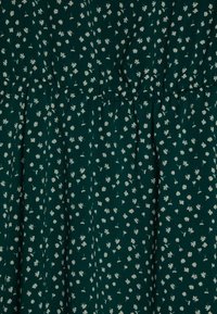 Ciemnozielony materiał z małym białym kwiatowym wzorem i marszczonym szwem tworzącym delikatne fałdy i fakturę.