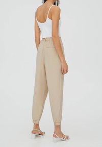 Beige tapschoenen met elastische boorden en een elastische tailleband, gecombineerd met een witte mouwloze top en witte sandalen met bandjes.