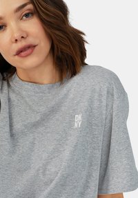Grijze katoen T-shirt met een ronde hals, korte mouwen en een klein, geborduurd wit logo op de linkerkant van de borst. Zachte textuur.