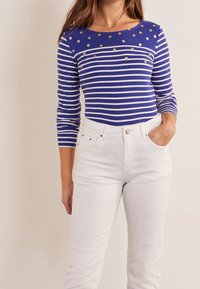 Blå och vit randig långärmad tröja med guldprickar på bröstet, kombinerad med högmidjade vita jeans. Mjuk tygkvalitet, figurnära design.