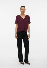 Bordeaux kortemouwen blouse met V-hals, knoopdetail en gerende mouwen, gecombineerd met zwarte rechte broek en bruine puntige schoenen.