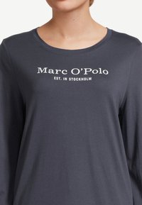 Långärmad, marinblå skjorta i mjuk bomull med vit tryckt text "Marc O’Polo EST. I STOCKHOLM" centrerad på bröstet.