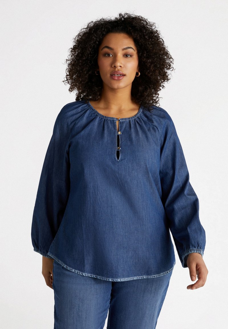 Camicia in denim con maniche lunghe, scollatura arricciata e patta con bottoni. Presenta una vestibilità ampia e un orlo curvo discreto. Colore blu scuro.