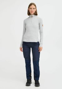 Lys grå langermet zip-up topp med ståkrage, kombinert med marineblå cargobukser med lommer og mørke detaljer. Svart fottøy fullfører antrekket.