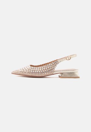 Beige slingback-kenkä, jossa matala paksu korko, kärjestä kärkinen varvas, aaltoileva reuna ja kimaltavat strassikoristeet.