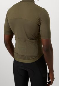 Maillot de cyclisme à manches courtes, vert olive, avec un haut texturé, une poche arrière zippée et une coupe ajustée. Ourlet ajustable pour le confort.