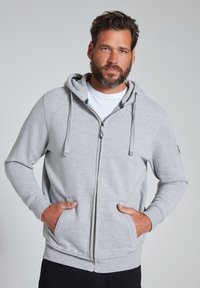 Felpa con zip grigio chiaro, dotata di zip frontale, stringhe e due tasche frontali. Caratterizzata da polsini e orlo a costine, texture morbida e cappuccio.