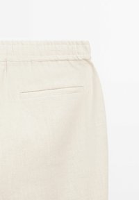Pantalon en lin beige avec une ceinture élastique et une poche passepoilée unique à l'arrière, côté droit.