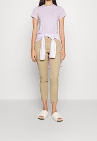 Ljuslila kortärmad t-shirt, beige åtsittande byxor och vita fluffiga slidesandaler. T-shirten är inslagen i en ljuslila skjorta.