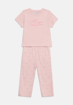 Ensemble de top manches courtes et pantalon rose clair avec un grand logo crocodile sur le haut et de petits motifs crocodile sur le pantalon.