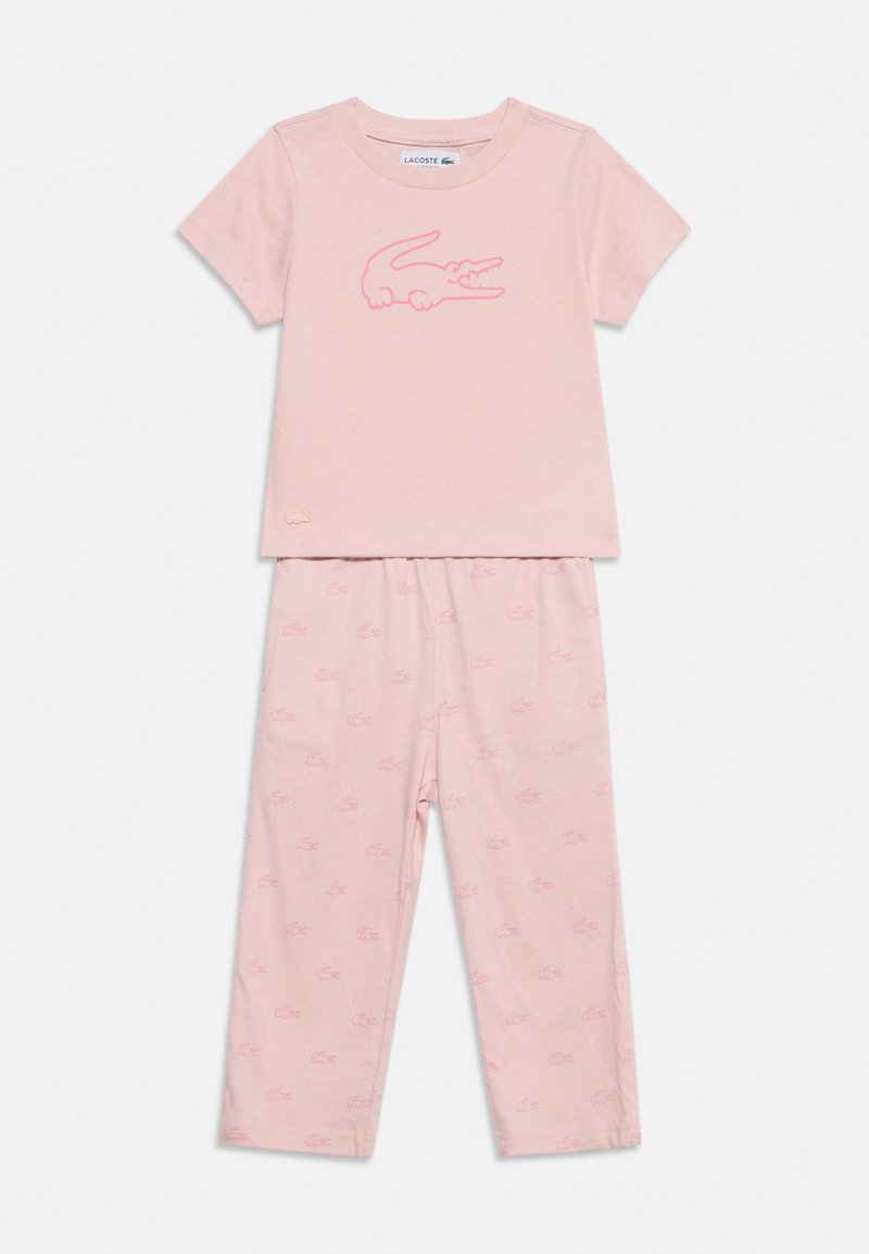Ensemble de top manches courtes et pantalon rose clair avec un grand logo crocodile sur le haut et de petits motifs crocodile sur le pantalon.