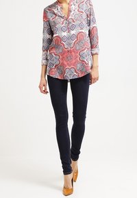 Bluse mit mehrfarbigem Paisleymuster, V-Ausschnitt und Dreiviertelärmeln, kombiniert mit dunklen Skinny-Jeans und beigefarbenen Absätzen.
