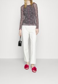 Maglietta a maniche lunghe nera e rosa con motivo, pantaloni bianchi su misura, sandali a scivolo rosa con fiori e una piccola borsa a tracolla nera.