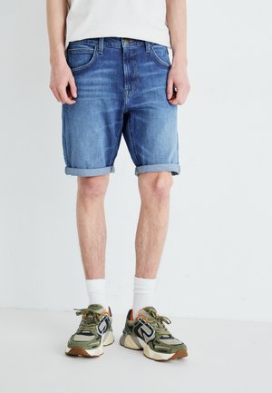 Shorts in denim azzurro chiaro, con risvolti, design a cinque tasche e vestibilità dritta. Abbinati a sneakers verdi e bianche.