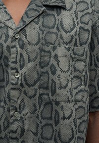 Πουκάμισο με κοντά μανίκια από υφασμάτινη ύφανση με γκρι και μαύρο σχέδιο ζώου, με τσέπη στο στήθος και κλείσιμο με κουμπιά.