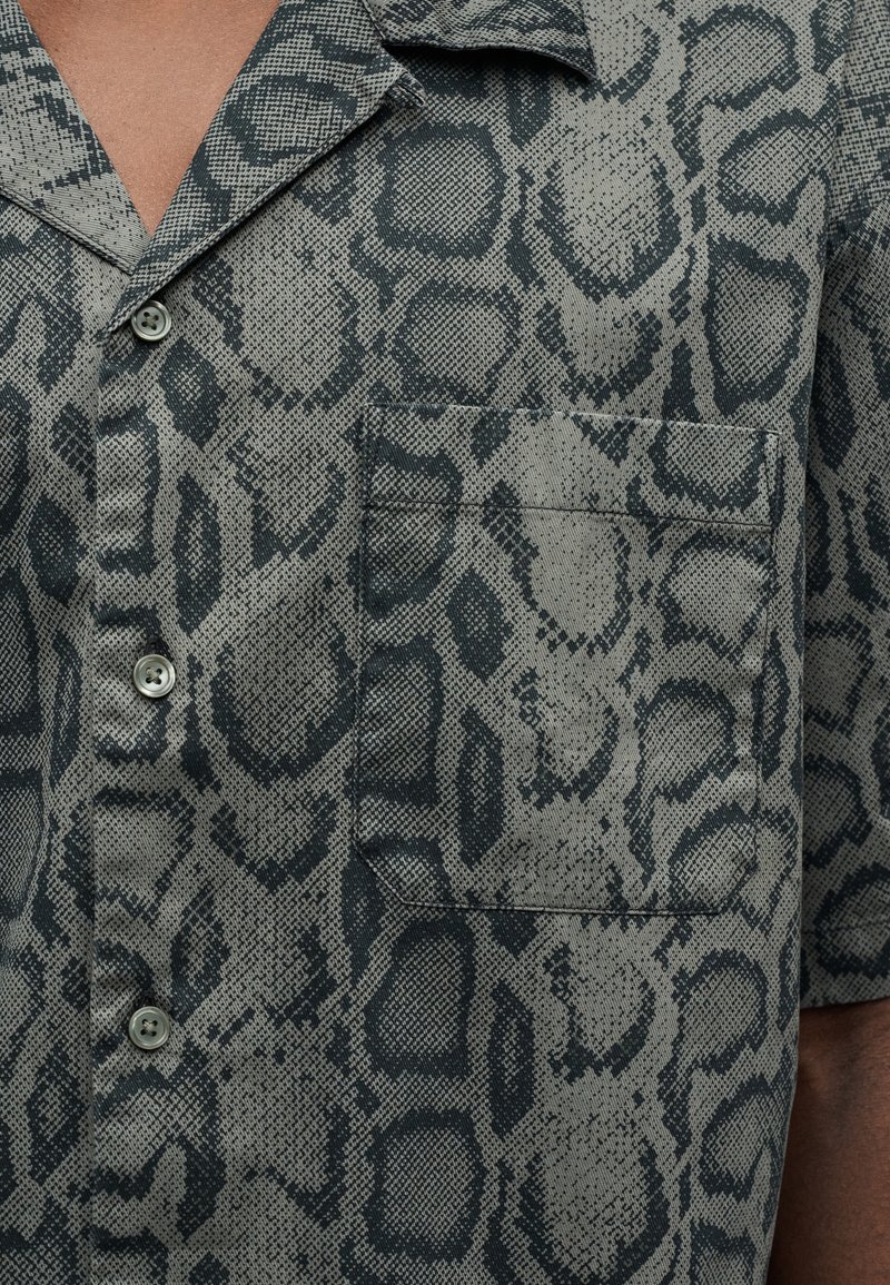 Camicia a maniche corte in tessuto strutturato con stampa animalier grigia e nera, dotata di taschino sul petto e chiusura con bottoni.