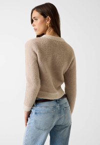 Maglione beige lavorato a maglia con finitura strutturata, scollo rotondo e maniche lunghe, abbinato a jeans in denim azzurro chiaro. Design minimalista.