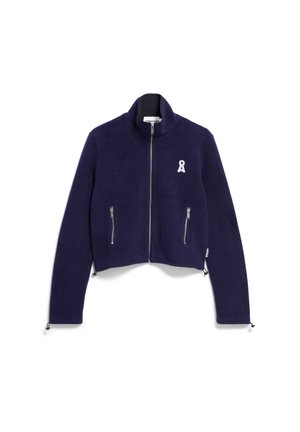 Veste courte en polaire bleu marine avec un col haut, deux poches avant zippées et un logo en ruban blanc. Présente des poignets élastiques et des ourlets ajustables.