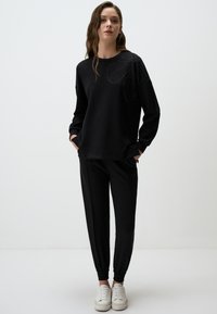 Felpa nera con un design floreale testurizzato in strass, abbinata a pantaloni neri a gamba affusolata e sneakers bianche. Tessuto liscio, vestibilità comoda.