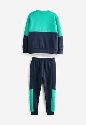 Ensemble de survêtement deux pièces en bleu marine et turquoise. Le sweat-shirt a une partie supérieure turquoise et une inférieure bleu marine, tandis que le pantalon présente des accents latéraux turquoise.