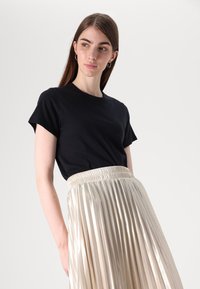 Tricou negru cu mânecă scurtă, asortat cu o fustă plisată metalizată aurie, având o talie elastică. Textură de material neted, design neutral.
