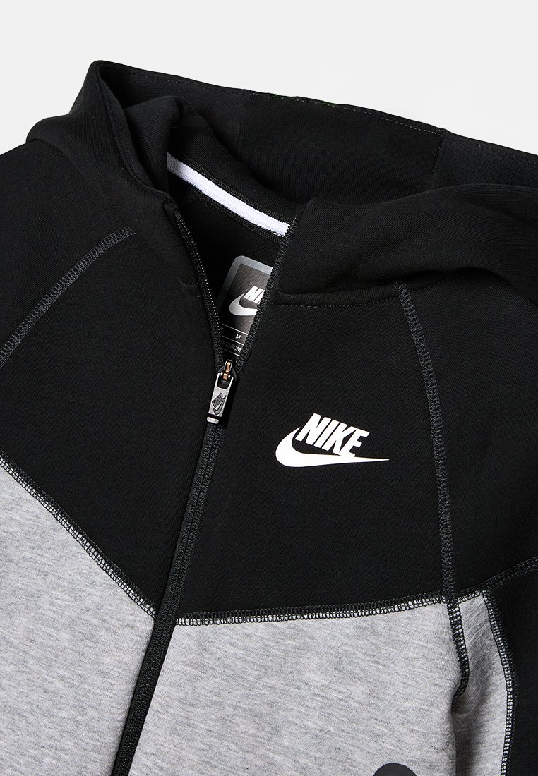 Nike zip-up hoodie met grijs en zwart kleurblokken, zachte stof, een capuchon en een wit logo op de borst, met een soepele rits.