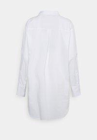 Camisa blanca de manga larga con cuello, pliegue en la parte posterior y puños con botones. Tejido suave con una textura ligeramente reflectante. Ajuste entallado, dobladillo curvado.
