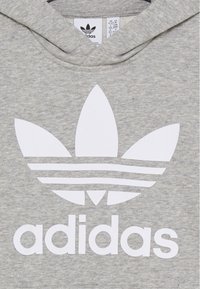 Sweat à capuche gris en tissu doux, arborant un grand logo Adidas blanc avec trois feuilles et trois bandes horizontales.