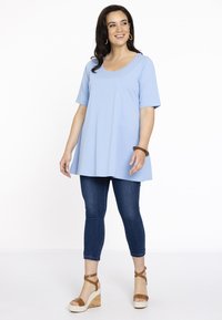 Lys blå kortærmet tunika med rund halsudskæring, parret med tætsiddende mørke denim jeans og brune kilehæle. Glat stof, afslappet pasform.