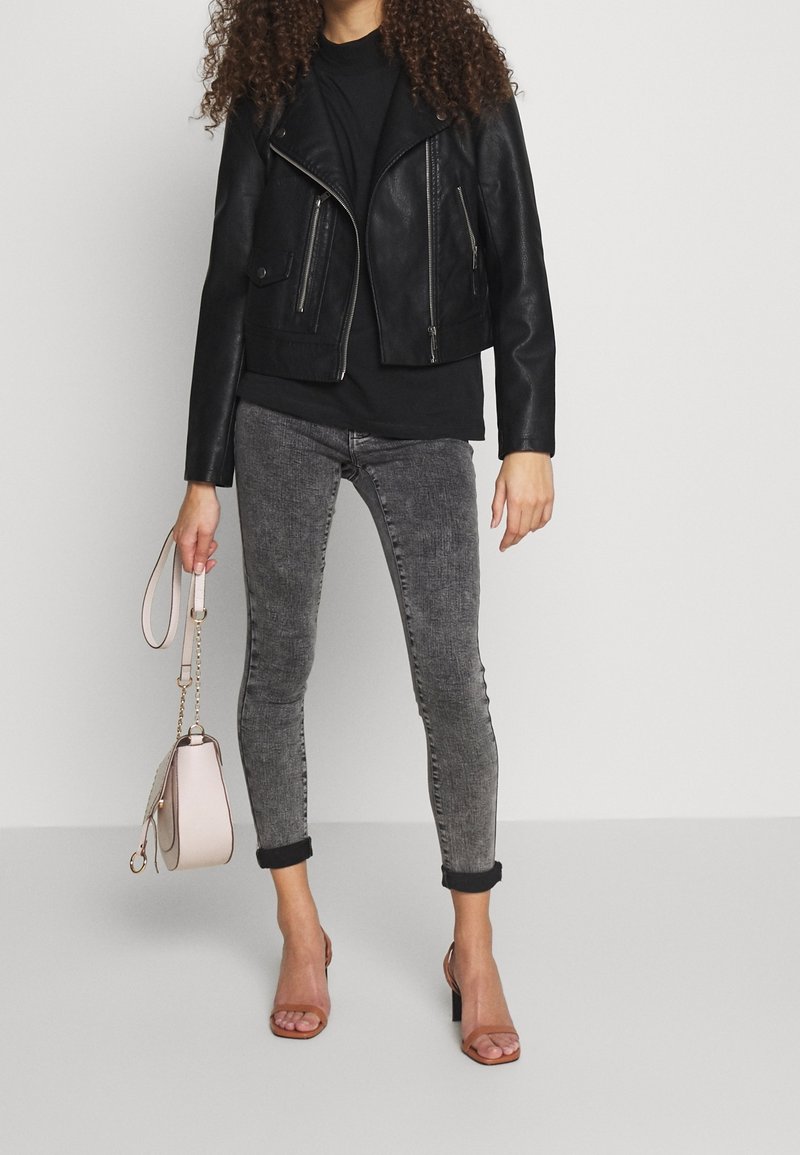 Zwarte leren motorjack met zilveren ritsen, gecombineerd met een zwart t-shirt en grijze skinny jeans. Houdt een lichtroze handtas vast.