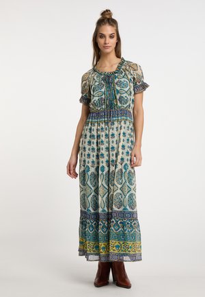 Maxikleid aus leichtem Stoff, mit einem floralen Muster in Blau und Grün, mit Rüschensäumen und elastischem Bund, kombiniert mit braunen Stiefeln.