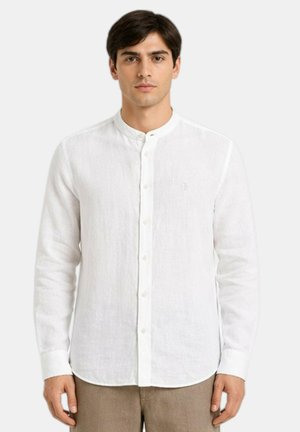 Uomo che indossa una camicia bianca con collo mandarino e maniche lunghe e pantaloni beige, in piedi contro uno sfondo bianco uniforme.