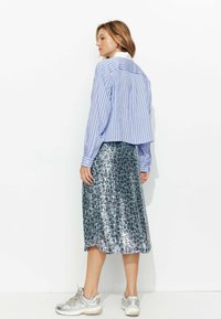 Chemise courte à rayures bleues et blanches associée à une jupe argentée en sequins longueur genoux et des baskets métalliques, avec une coupe décontractée et une texture plissée.