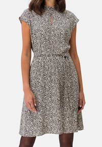 Zwart-wit gestreepte jurk met een hoge kraag, korte mouwen en een sleutelgatopening bij de hals, strakker aan de taille.