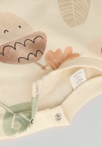 Kremowy bodysuit z materiału, zdobiony zabawnymi wzorami liści i zwierząt w ziemistych odcieniach, z zatrzaskami na dole ułatwiającymi zakładanie.