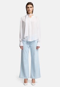 Blusa di seta bianca con cravatta e maniche lunghe, abbinata a jeans a gamba larga blu chiaro e scarpe con tacco bianche.