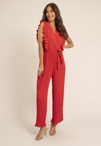 Combinaison rouge plissée avec des manches froncées, décolleté en V et ceinture à nouer à la taille. Présente des jambes larges et une texture lisse.