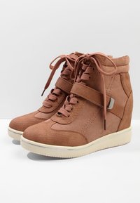 Hnědé klínové tenisky s texturovanou špičkou a patou, zavazováním na tkaničky a suchým zipem na bílé podešvi, zobrazené na jednobarevném pozadí.