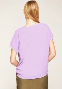 Levandulové tričko s krátkým rukávem, volného střihu a kulatým výstřihem, s světlým lemem podél manžet a spodního lemu.
