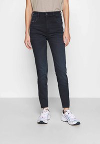 Mörka denim skinny jeans med hög midja, fem fickor, subtila sömnadsdetaljer och en slät yta. Matchas med vita sportskor.
