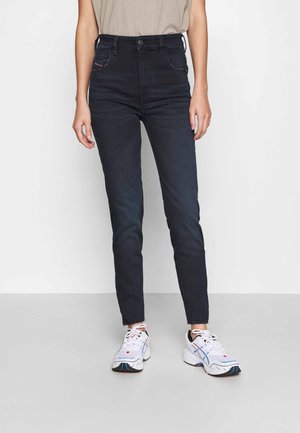 Jeans skinny de mezclilla oscura con cintura alta, que cuentan con cinco bolsillos, detalles de costura sutiles y una textura suave. Combinados con zapatillas deportivas blancas.