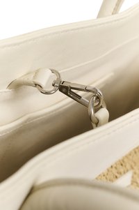 Εσωτερικό λευκής τσάντας με μεταλλικό κούμπωμα που συνδέει δύο κυκλικά δαχτυλίδια σε δερμάτινο λουράκι.