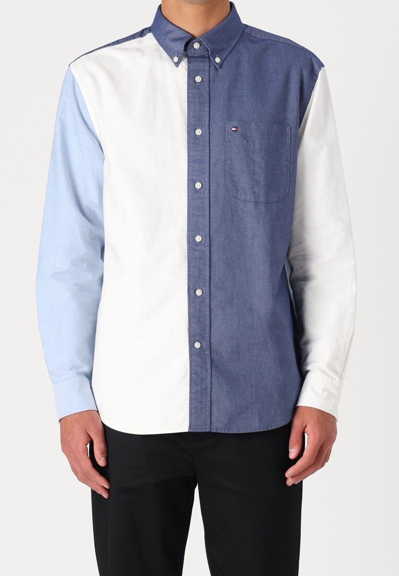 Camicia con bottoni caratterizzata da un design a blocchi di colore con sezioni azzurro chiaro, bianco e blu scuro. Tessuto di cotone liscio, con una tasca sul petto.