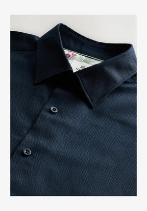 Marineblå skjorte med knapper, der har et geometrisk mønster, tekstureret stof og en foldet krave med kontrasterende inderside. To sorte knapper er synlige.