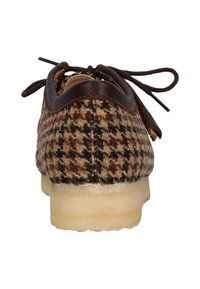 Ruskea houndstooth-kuvioinen kenkä, jossa on teksturoitu päällinen, ruskeat nahka-akcentit ja kermaisen värinen kumipohja. Nyörit näkyvät ylhäällä.