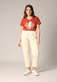 Roestkleurig t-shirt met een metallic gouden bliksemhart graphic; crèmekleurige corduroy broek met een elastische tailleband en textuur stof.