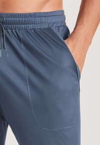 Middelblauwe sportshorts van stof met een elastische tailleband, trekkoord en zijzakken. Glad materiaal en minimale stikdetails.