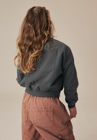 Mørkegrå cropped sweatshirt med en samlet søm, parret med lyserøde cargo bukser med sidelommer og en afslappet pasform.